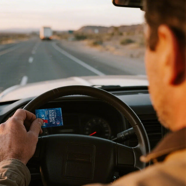 Person driving a car on a desert road with a clear sky, holding a STIM Energy Strip